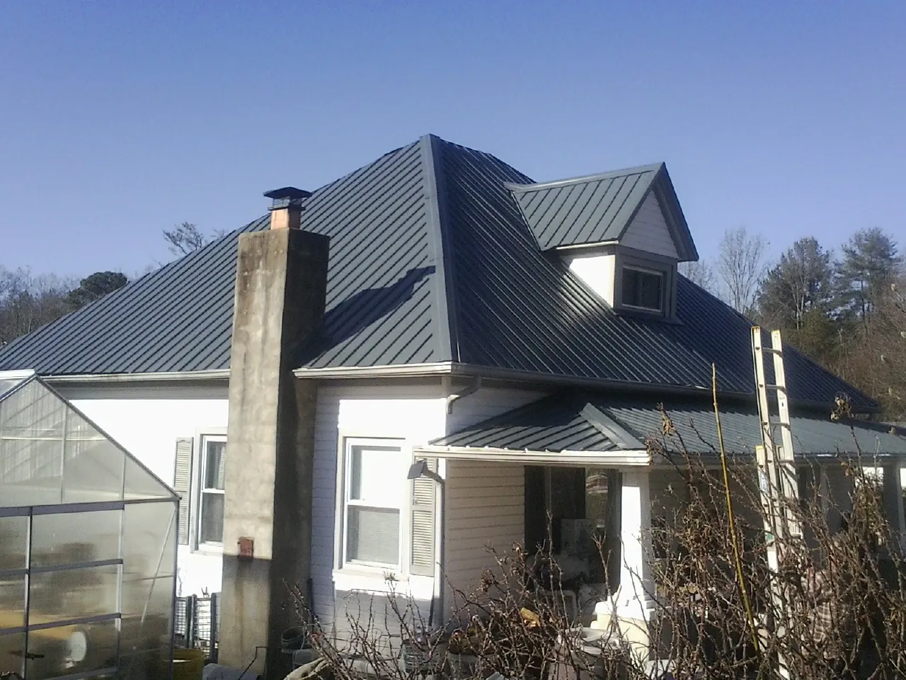 Dark blue standing seam metal roof on a white farmhouse with dormer — Slate & Tile Roof Repair by Roofing Brothers in Hillsdale