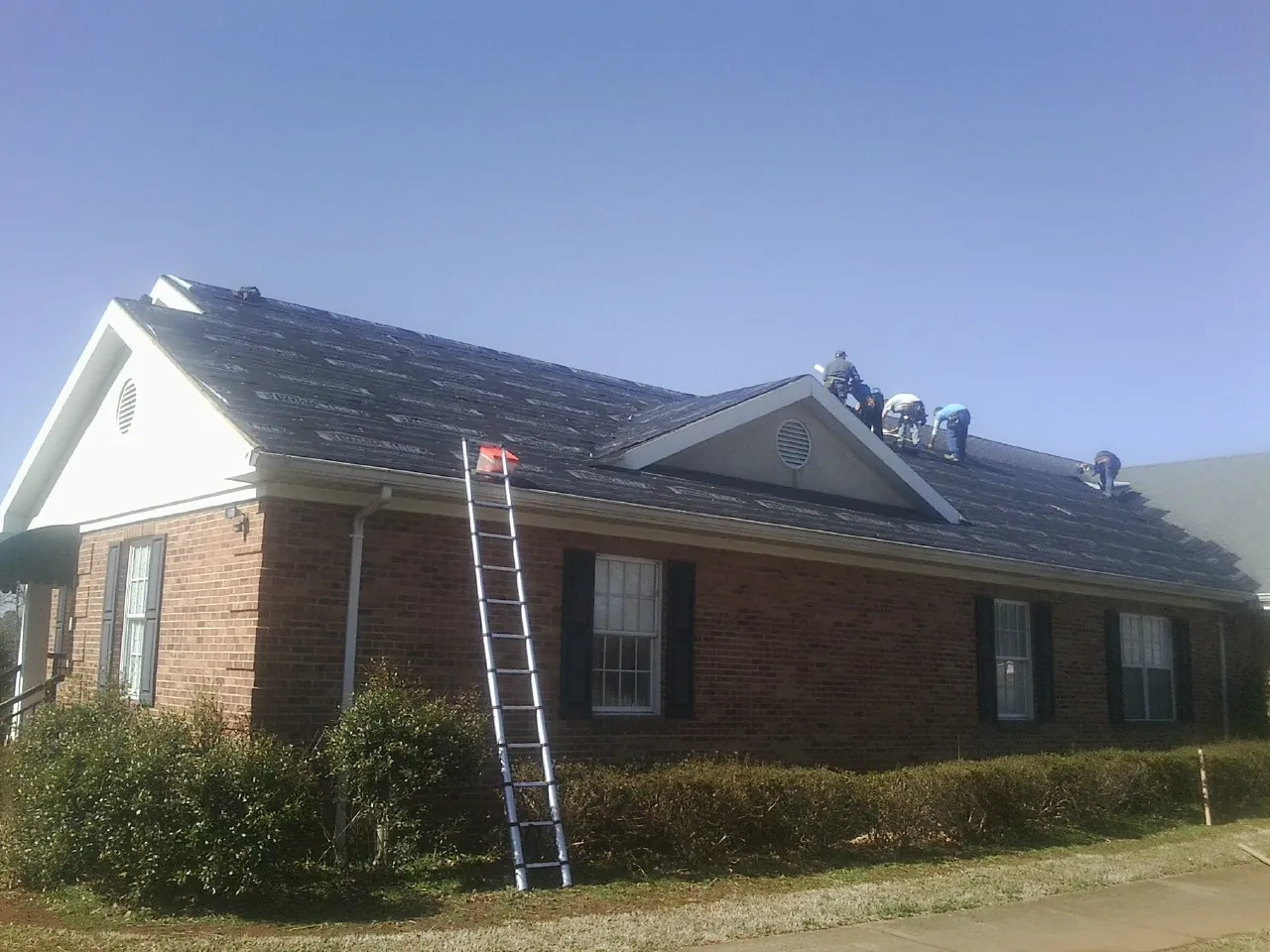 Crew tearing shingles off a brick ranch roof with a ladder set — Metal Roof Repair work by our crew in Hillsdale